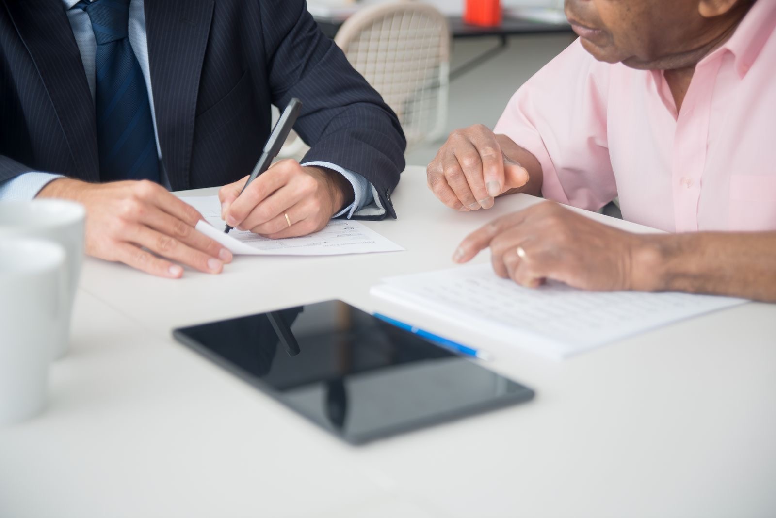 Two people signing a printed agreement across a desk
